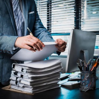 An entrepreneur organises documents at his desk with his laptop open and under time pressure,