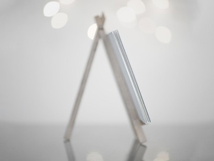 Mini easel in white made of wood, standing on a reflective smooth surface, white background with