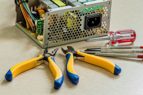 Side view of opened desktop power supply together with pliers and screwdrivers needed to repair