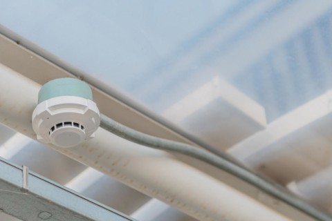 Electronic smoke detector on ceiling of enclosed pedestrian walkway with blurred plexiglass window