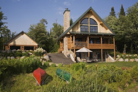 Garage and handcrafted two story spruce log home cabin with fieldstone chimney, green sheet metal