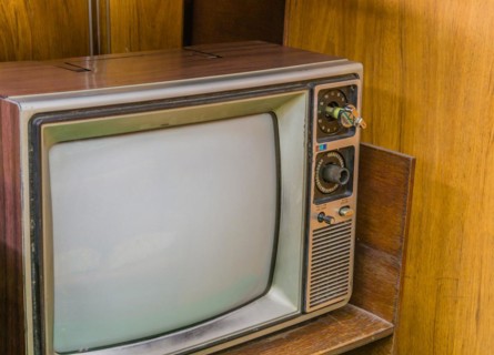 Old nineteen inch television set with wood grain chassis sitting on wooden desk. Located in an old