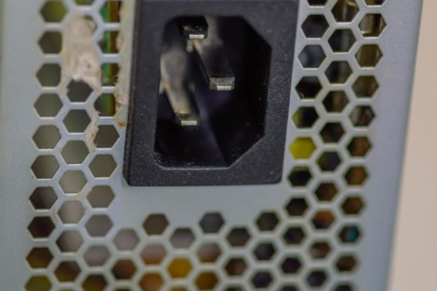Side view of used computer power supply with focus on male pins of plug that attaches to power cord