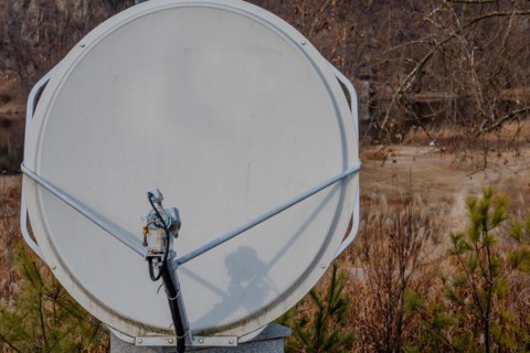 Closeup of satellite dish mounted on concrete column with riverside slightly blurred in background