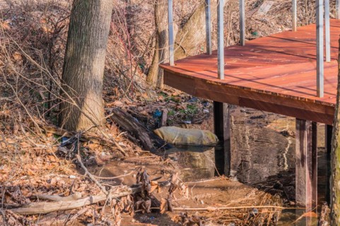 A raised deck beside a creek with a blue barrel partially hidden underneath, in South Korea