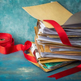 Pile of documents wrapped in red ribbon next to an open brown envelope on wooden surface, symbol