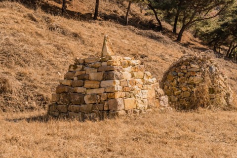 Two pyramid shaped rock structures in field of brown grass at foot of hillside in Boeun, South