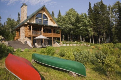 Handcrafted two story spruce log home cabin with fieldstone chimney, green sheet metal roof and red