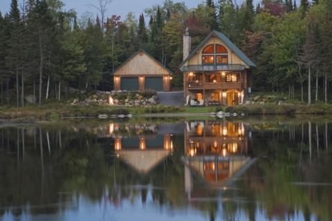 Illuminated two car garage and handcrafted two story spruce log cabin home with fieldstone chimney