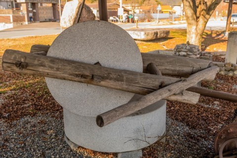 Old antique millstone and wheel in covered shelter with mountain community in background in South