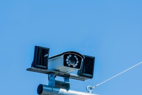 Closeup of closed circuit camera mounted on metal pole against light blue sky in background in