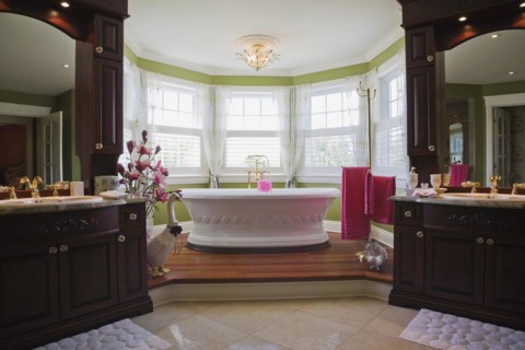 Master bedroom en suite with freestanding white bathtub on raised platform and his and her vanities