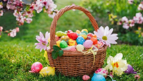 A festive Easter basket filled with colourful eggs, surrounded by spring flowers in the grass,