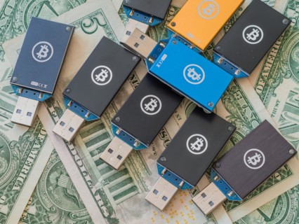 Multiple cryptocurrency USB hardware wallets spread over US dollar bills, in South Korea