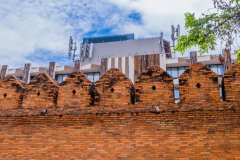 Ancient style brick wall with modern structures and cell towers behind, in Chiang Mai, Thailand,