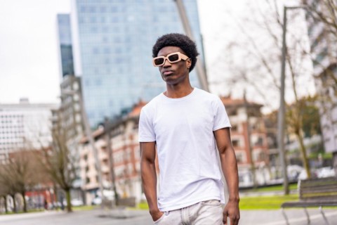 Confident cool and young african man in white clothes and sunglasses walking along the city