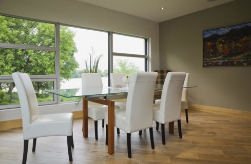 Clear glass top table with white leather high back chairs in dining room with beige ceramic tile