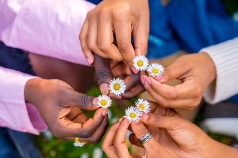 Top view of three unrecognizable african young female friends holding flowers and putting together