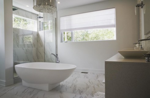 Glass shower stall with white acrylic freestanding bathtub in main bathroom with marble floor tiles
