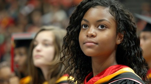 A latino young girl in school graduation attire looks forward with a serious expression amid a