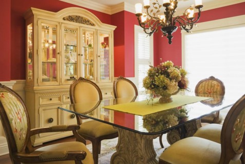 Glass top table with high-back wooden and upholstered chairs in dining room with buffet inside