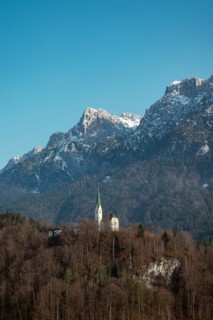 St. Niklaus Church in front of the snow-covered Zahmer Kaiser, surrounded by forest under a clear