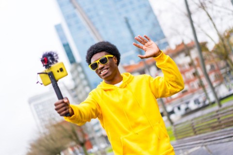 Cool african young content creator waving at camera steaming live standing in a city