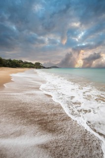 Lonely, wide sandy beach with turquoise-coloured sea. Tropical plants in a bay at sunset in the