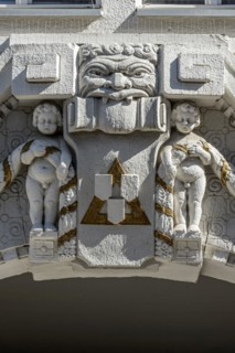 Decorative figures above gateway in Art Nouveau style, naked boys with garland, grim male face,
