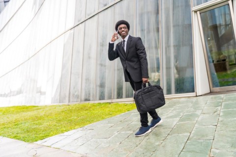 Full length portrait of a cool african businessman talking to the mobile walking in the city