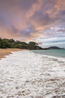 Lonely, wide sandy beach with turquoise-coloured sea. Tropical plants in a bay at sunset in the