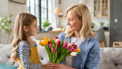 A little girl presents her smiling mother with a colourful bouquet of tulips in the cosy living