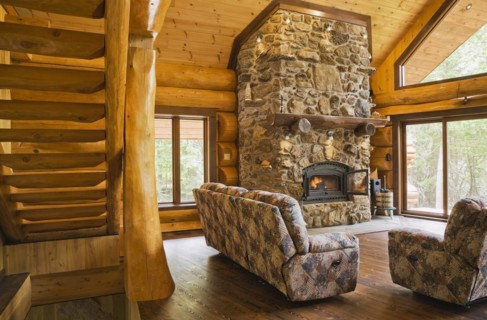 Wooden log stairs and upholstered sofas with lit fieldstone and porous rock fireplace in living