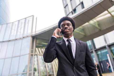 Low angle view portrait of a young busy african businessman talking to the mobile while commuting