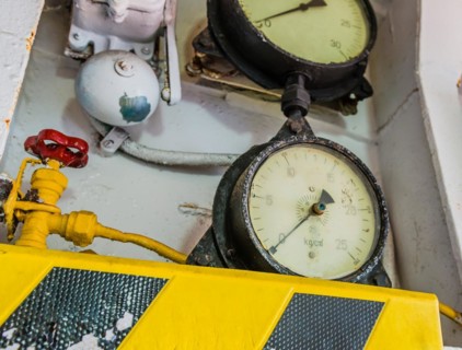 Old pressure gauges mounted above yellow and black striped ledge with valves and bell in background