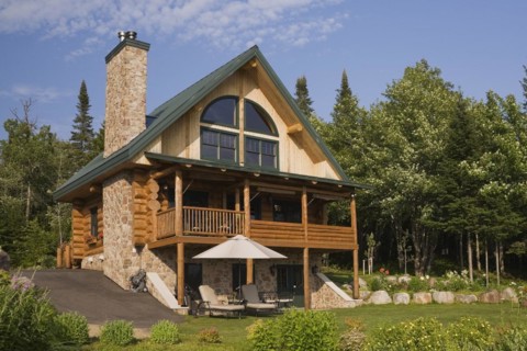 Handcrafted two story spruce log home cabin with fieldstone chimney and green sheet metal roof in