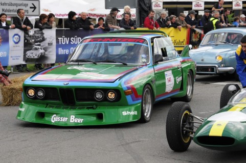 A green racing car with the number 141 drives on a road, surrounded by spectators, SOLITUDE REVIVAL