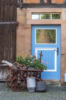 Curious decoration on a front door, flower pot, geraniums, old wagon with firewood, milk can and