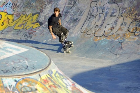 A skateboarder prepares to perform a trick in a half-pipe against the light of the evening sun,
