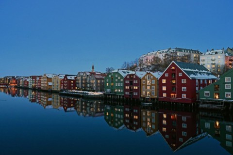 Historic warehouse buildings reflected in the river Nidelva at dusk, Bryggene, Trondheim, Norway,