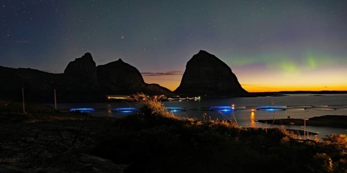 Northern lights (aurora borealis) mingle with sunset, sea, striking mountains and fish farm,