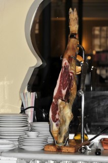 Jaen, A Jamon Iberico on a wooden board next to a pile of plates in a restaurant, Jaen, Andalusia,