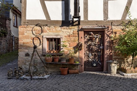 Old half-timbered house, whimsically decorated, stone towers, tripod with pendulum, flower pots,
