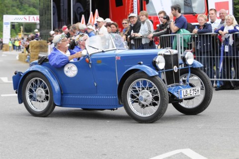 A blue vintage sports car drives past a fence, driver and passenger in the cockpit, SOLITUDE