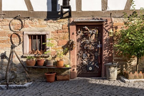 Old half-timbered house, whimsically decorated, tripod with pendulum, flower pots, door with masks,