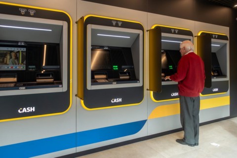 Elderly man collecting money from indoor ATM cash dispenser of bank neutral Bancontact CASH point