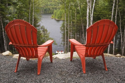 Two bright red plastic Adirondack chairs overlooking a calm lake through Betula, Birch trees with