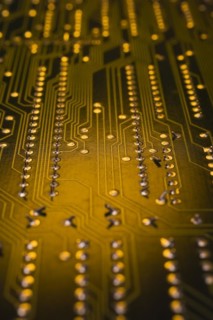Close-up of golden yellow lighted electronic computer circuit board with lines and silver solder