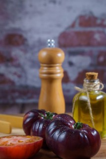 Group of tasty fresh tomatoes of the blue variety together with wooden tongs, a glass bottle of