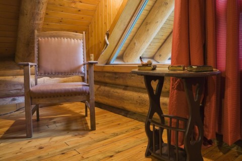 Brown wooden leather armchair and side table in master bedroom with red curtains and wood plank